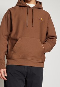 Felpa con cappuccio marrone, dotata di tasca frontale e con un piccolo logo color marrone. Realizzata in tessuto morbido, con una vestibilità comoda e polsini a coste.