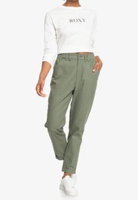 Pantalon vert en mélange de coton à coupe décontractée, doté d'une fermeture à boutons sur le devant, de poches lat érales et de revers roulés, associé à un haut blanc avec le logo Roxy.