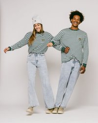 Grønne og hvite stripete langermede skjorter, lyseblå vide jeans, og beige sko. Tilbehøret inkluderer en grå lue. Modellene poserer sammen.