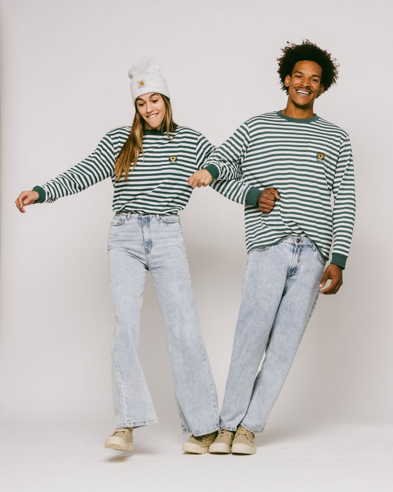 Grønne og hvite stripete langermede skjorter, lyseblå vide jeans, og beige sko. Tilbehøret inkluderer en grå lue. Modellene poserer sammen.