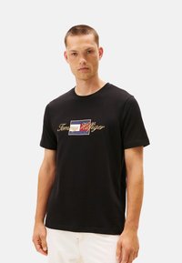 Camiseta de algodón negra con un logo bordado multicolor en el centro. Cuello redondo clásico y mangas cortas. Textura suave.