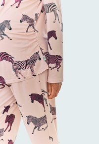 Hellrosa Loungewear-Set mit einem Zebramuster in dunklen und hellen Farbtönen. Der Stoff wirkt weich und hat eine lockere Passform mit seitlicher Raffung.