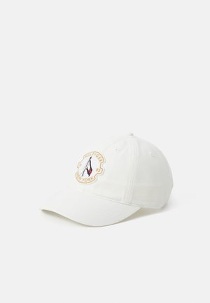 Boné de beisebol branco feito de tecido, com um logotipo bordado circular que apresenta um veleiro, detalhes em vermelho, branco e azul, e uma fita ajustável.
