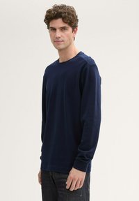Dunkelblauses Langarmshirt mit rundem Ausschnitt, aus einem glatten Stoff gefertigt. Hat einfache Nähte und eine lockere Passform. Eignet sich für den Freizeitlook.