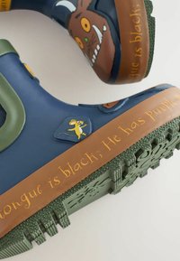 Gummistiefel in Marineblau und Braun. Mit einem grünen Akzent und verspielten Grafiken einer Maus und eines Monsters. Der Text auf der Sohle ist gelb.