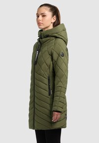 Olívazöld, steppelt parká, kapucnival, átlós chevron mintával, cipzáras zsebekkel és logóval ellátott folttal az ujjon.