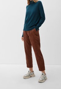 Haut à manches longues bleu sarcelle, pantalon en velours côtelé rouille et baskets chunky avec un design blanc, gris et noir. Texture lisse et coupe décontractée.