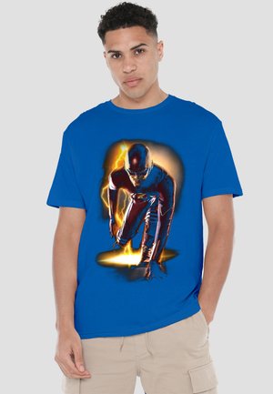 Young man wearing blue t-shirt with graphic of a superhero in red suit crouching, surrounded by yellow lightning effects.