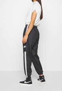 Black athletic pants with white side stripes, elastic waistband, and drawstring. Paired with a plain white short-sleeve top and black high-top sneakers.