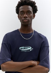 Navy blue t-shirt made of cotton, featuring a logo with light blue text and a starburst graphic; short sleeves and relaxed fit.