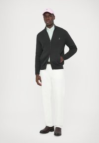 Tmavosivý rebrovaný kardigán so zipsom vpredu, nosený cez svetlozelenú pruhovanú košeľu, v kombinácii s bielymi nohavicami a čiernymi čižmami. Súčasťou je ružová čiapka.