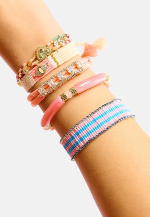 Quatre bracelets au poignet : tissu tissé rose et beige, accents de strass, plastique lisse rose, et un motif de perles bleu et rose.