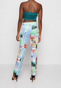 Crop top en satin vert avec des bretelles croisées, associé à un pantalon ajusté à motifs colorés comprenant un mélange de graphiques et de formes. Chaussures à talons.
