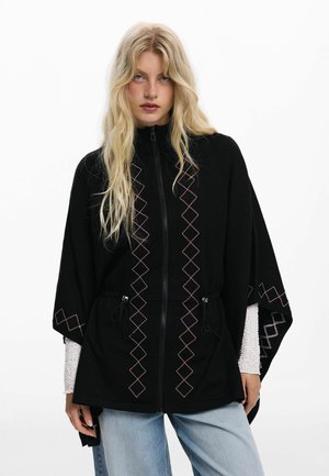 Black zip-up outerwear with a relaxed fit, featuring pink diamond pattern embroidery and drawstring details, paired with light blue jeans.