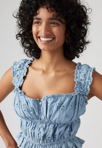 Robe en coton bleu clair avec des bretelles à volants, des motifs floraux brodés, une taille froncée et un détail de boutons à l'avant.
