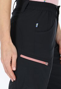 Black outdoor pants made of textured fabric, featuring a pink zipper pocket and a small blue and yellow flag tag on the side.