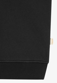 Schwarzes Sweatshirt-Material mit glatter Textur, geripptem Saum und einem kleinen beigen Markenetikett an der Seite. Schlichtes, minimalistisches Design.