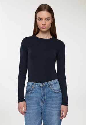 Maglietta a maniche lunghe in maglia blu navy con scollatura rotonda, abbinata a jeans a vita alta di un blu chiaro con chiusura classica a bottone e zip.