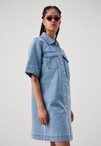 Denim skjortekjole i lyseblå, med knappelukking foran, korte ermer, to brystlommer og en rett, avslappet passform.