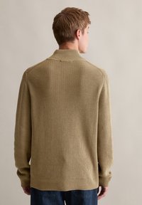 Beige gestrickter Pullover mit hohem Kragen, gerippter Textur und langen Ärmeln. Der Saum und die Bündchen sind ebenfalls gerippt und bieten ein strukturiertes Design.