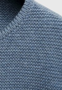 Svijetloplavi pleteni materijal s teksturiranom površinom i rebrastim detaljem ovratnika. Tkanina izgleda labavo i mekano.