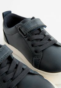 Donkerblauwe leren sneakers met gestructureerde veters, elastische band en witte rubberen zolen. Voorzien van gestikte accenten en een gewatteerde binnenkant.