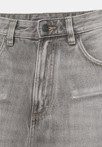Gros plan sur un jean en denim gris délavé montrant un bouton, des passants de ceinture et des poches avant avec des détails de couture visibles.
