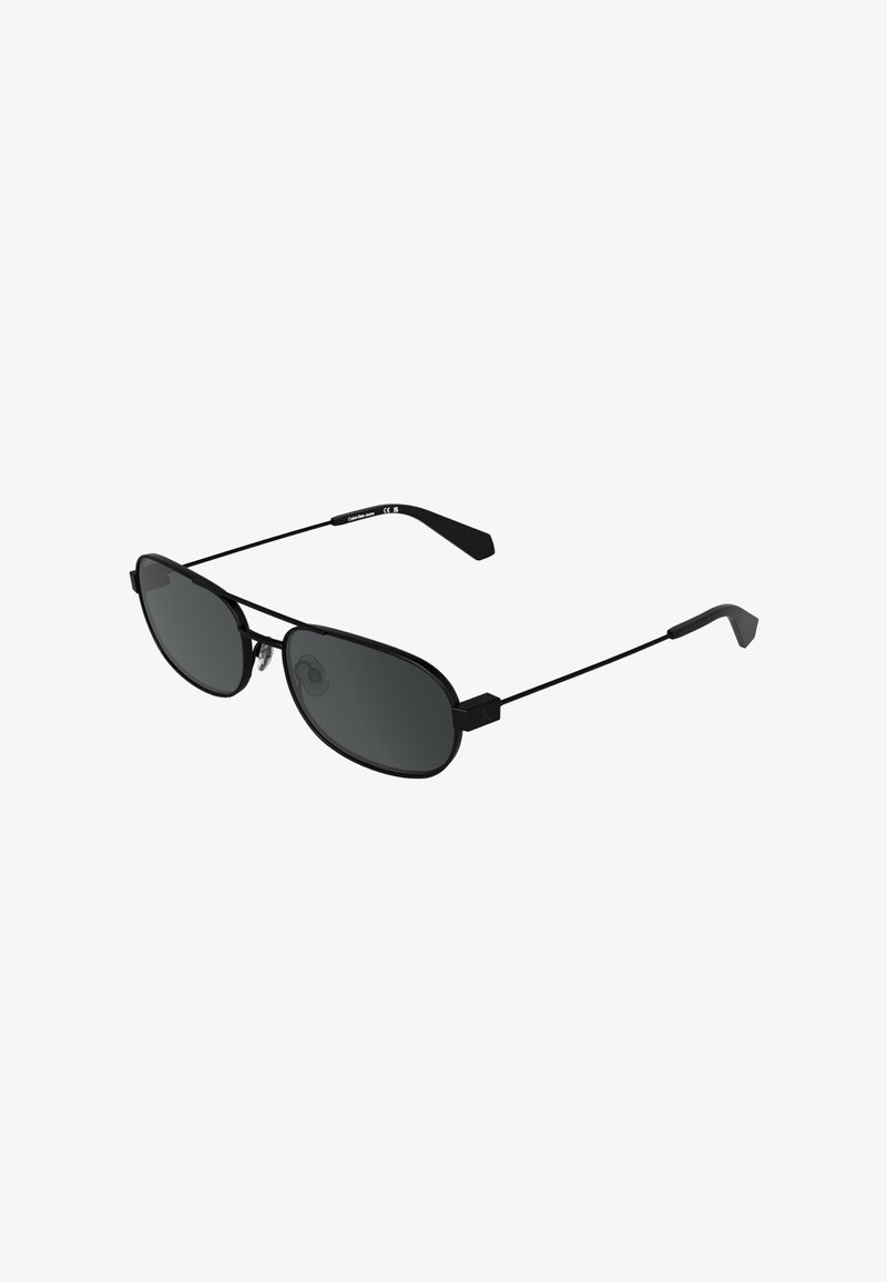 Lunettes de soleil noires à forme ovale des verres, monture en métal et branches fines. Verres teintés foncés offrant une couverture complète. Design minimaliste souligné par un accent métallique.