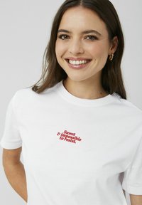 T-shirt en coton blanc avec du texte brodé rouge, "Doux & impossible à résister," décalé sur la poitrine, manches courtes.