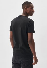 Tricou negru din bumbac cu guler rotund, mâneci scurte și o siluetă ajustată, expus din spate pe un fundal alb.