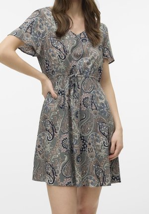 Femme portant une robe à manches courtes, longueur genou, imprimé paisley, taille froncée avec un cordon à nouer.