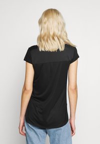Svart kortärmad skjorta med en slät yta och rundad nederkant. Har en synlig bakpanel med en lätt veckdetalj.