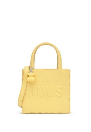 Bolso rectangular amarillo con asas superiores, una correa para el hombro, logo "TOUS" en relieve y un pequeño colgante con forma de oso unido al asa.