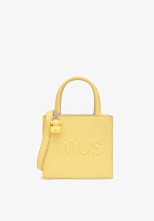 Yellow rectangular handbag with top handles, a shoulder strap, embossed "TOUS" logo, and a small bear-shaped charm attached to the handle.