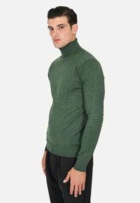 Maglione verde a collo alto realizzato in tessuto morbido, design aderente, maniche lunghe e polsini e orlo a costine, abbinato a pantaloni neri.