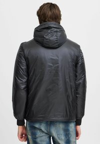 Schwarze, kapuzengetragene Jacke mit glatter, glänzender Textur. Elastische Bündchen und Saum. Rückansicht zeigt ein schlichtes Design ohne sichtbare Muster oder Logos.