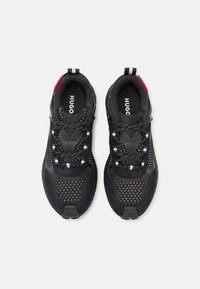 Black athletic shoes with a mix of suede and mesh. Features reflective detailing, adjustable laces, branding on the insole, and a red accent.