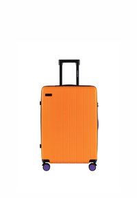 Pomarańczowa walizka z twardą obudową z pionowymi żłobieniami, wysuwanym czarnym uchwytem i fioletowymi kółkami, zaprojektowana dla ułatwienia mobilności.