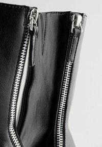Stivale alla caviglia in pelle nera con zip argentate su entrambi i lati, caratterizzato da una finitura texture e un design slanciato.