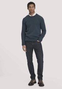 Marineblaues Strickoberteil mit Rundhalsausschnitt, kombiniert mit dunklen Jeans und braunen Schnürstiefeln. Der Pullover hat eine gerippte Struktur an den Bündchen und dem Saum.