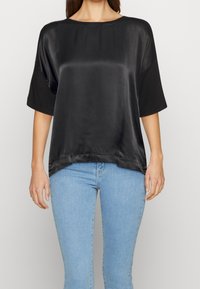 Camicia nera in satin con maniche corte, scollatura rotonda e vestibilità ampia. Il tessuto ha una texture liscia e lucida e un orlo curvo.