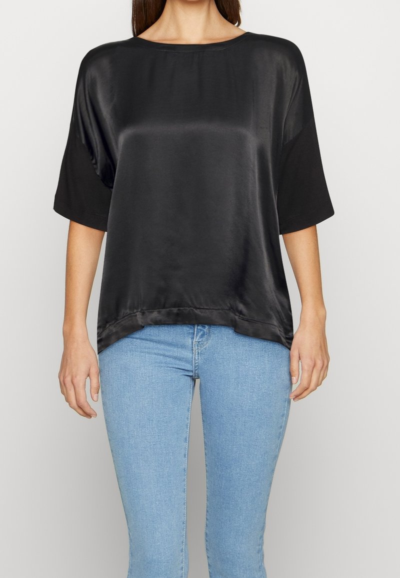 Camicia nera in satin con maniche corte, scollatura rotonda e vestibilità ampia. Il tessuto ha una texture liscia e lucida e un orlo curvo.