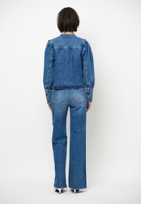 Denimjack en broekset in een medium blauwe wassing. De jas heeft opgezette mouwen, een logo detail op de rug en standaardzakken. Fittend silhouet.