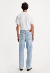 Ljusblå denimjeans med avslappnad passform, raka ben, två bakfickor och ett brunt lädermärke på midjan.