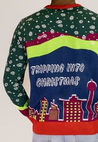 Strickpullover in Grün, Rot und Blau. Verfügt über Smiley-Muster, den Text "TRIPPING INTO CHRISTMAS" und ein Stadt-Skyline-Design auf der Rückseite.