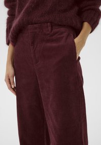 Bordeauxkleurige corduroy broek met verticale ribbels, voorzien van zijzakken en een klassieke pasvorm. Het materiaal heeft een gestructureerde uitstraling.