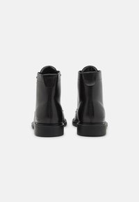 Botines de cuero negro con una textura suave, punta redondeada y tacón bajo en bloque. Presentan costuras mínimas y una lengüeta en la parte trasera.