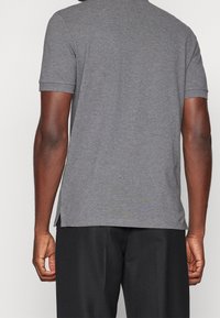 Camiseta gris de manga corta con un corte relajado, tejido texturizado y aberturas laterales para facilitar el movimiento, combinada con pantalones oscuros.