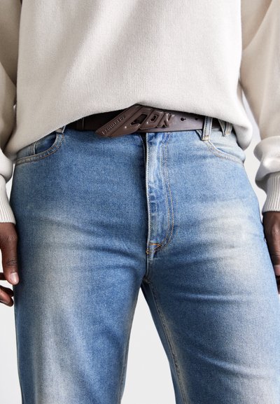 Lyseblå denimjeans med falmet tekstur og kontrasterende oransje søm. Et mørkebrunt belte med preget tekst sikrer livet.