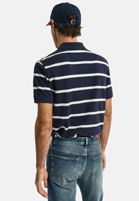 Polo a righe blu navy con righe orizzontali bianche, dotato di colletto e maniche corte, abbinato a jeans in denim blu chiaro.